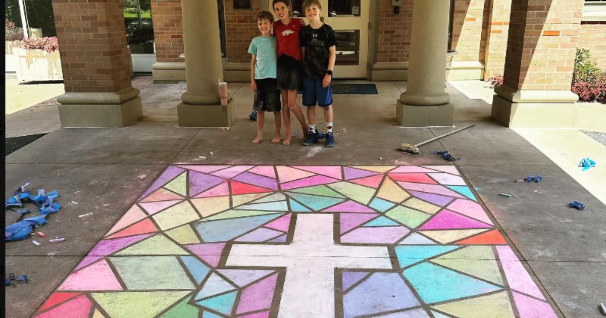 Children stand behind a chalk cross, which is set against a drawing of a stained-glass window outside of the governor's mansion in Arkansas.