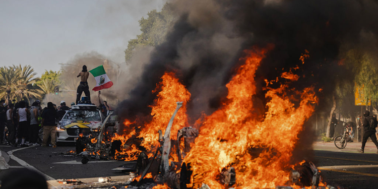 Protesters Photographed Holding Mexican Flag in Front of Burning Vehicle